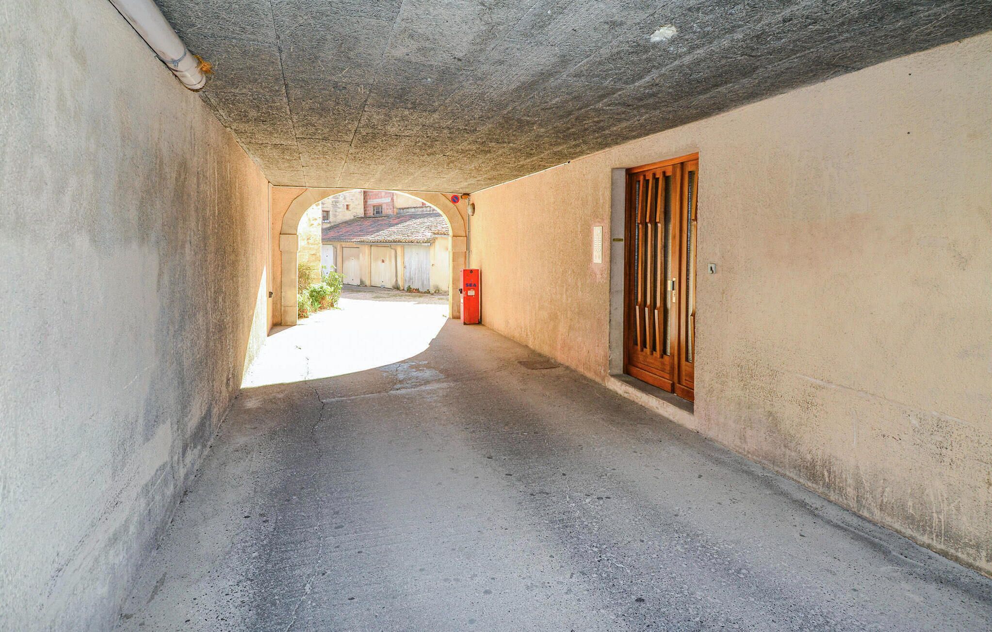 Une ruelle étroite avec un plafond en béton, une porte en bois sur la droite et une boîte aux lettres rouge au loin.