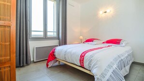 A bedroom with a bed, a window with curtains, a wall-mounted light, and a radiator. - Beautiful apartment in Uzès with WiFi (Uzès)