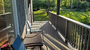 Une véranda abritée, avec deux chaises et une table, donnant sur une pelouse bien entretenue et des arbres.