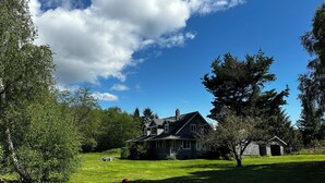 Une maison avec une grande pelouse, un ballon rouge et un ciel bleu dégagé.