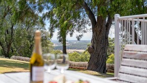 A table with a bottle and glasses, overlooking a scenic landscape with trees and a view of the countryside. - Moondyne Estate Augusta with Pool, Tennis Court and Ocean Views (Deepdene)