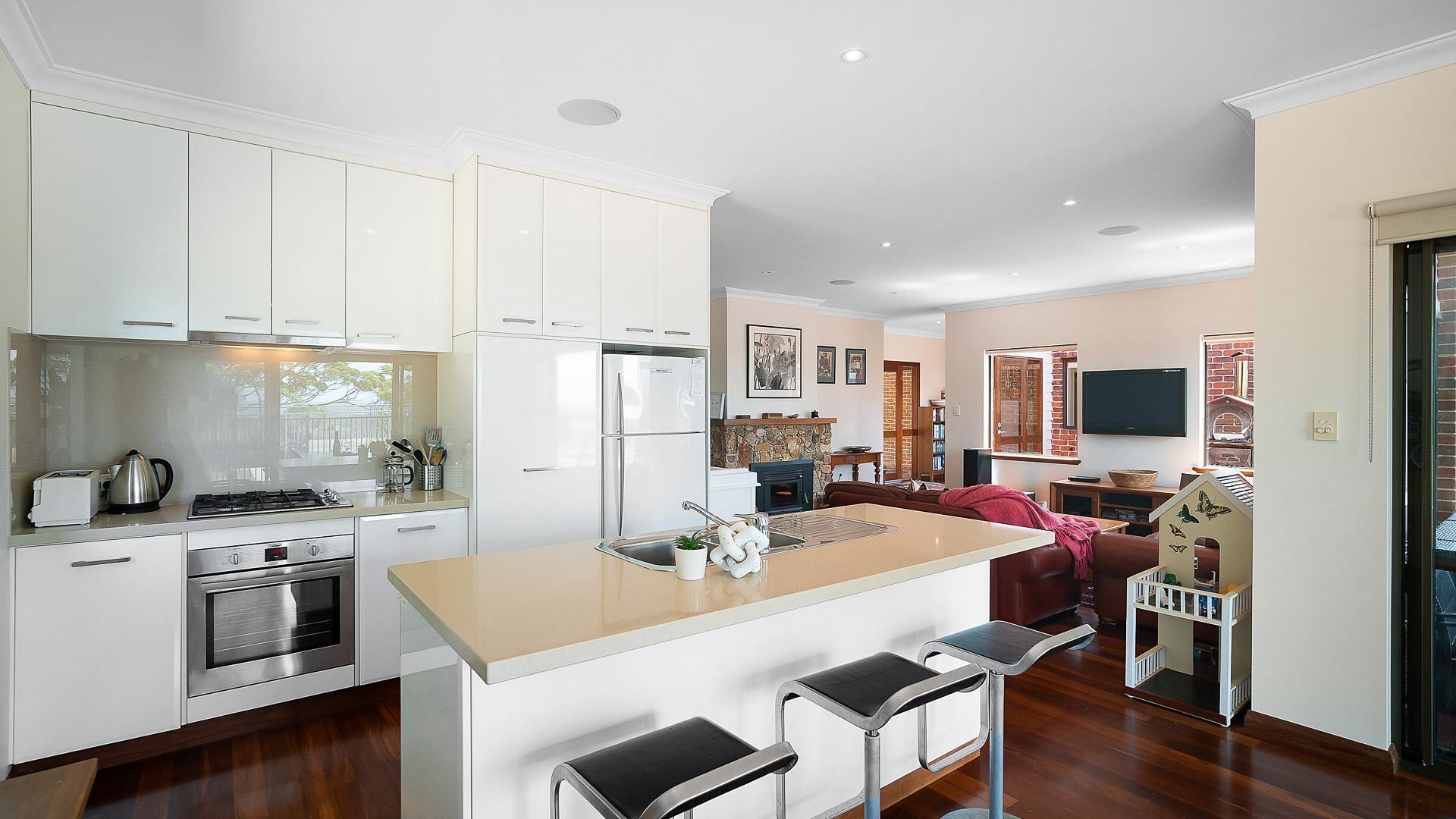 Une cuisine moderne avec des meubles blancs, un îlot central doté de tabourets, un four encastré et une cuisinière.