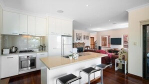 A modern kitchen with white cabinetry, a central island with bar stools, a built-in oven, and a stove. - Moondyne Estate Augusta with Pool, Tennis Court and Ocean Views (Deepdene)