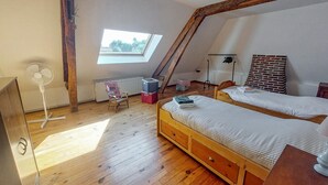 Ein Schlafzimmer mit zwei Holzbetten, einem Oberlicht, einer Heizung, einem Ventilator und einer Ziegelwand.