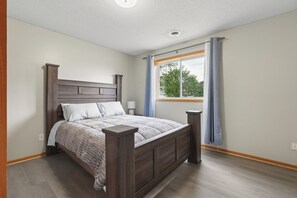 Une chambre Ă coucher avec un lit en bois, une fenĂȘtre avec des rideaux, une table de chevet et un luminaire au plafond.