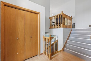 Une porte Ă deux battants en bois, un escalier en bois avec une rampe et une petite table avec une chaise.