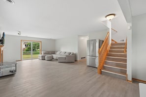 Amplia sala de estar con un sofá seccional grande, una escalera de madera y una puerta de cristal que da a un balcón.