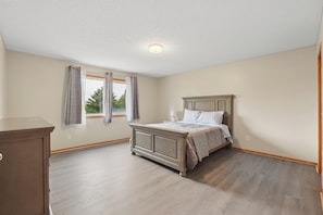 A bedroom with a bed, a window with curtains, a dresser, and a ceiling light.
