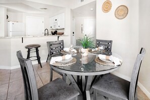 A dining area with a round glass table set for four, surrounded by grey upholstered chairs. - Desert Oasis 2BD/2BA Gated Resort ~ Pool ~ Gym ~ Pet Friendly ~ BBQ (Phoenix)