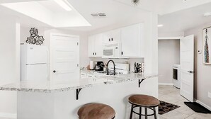 Una cocina moderna con armarios blancos, encimera de mármol y dos taburetes.