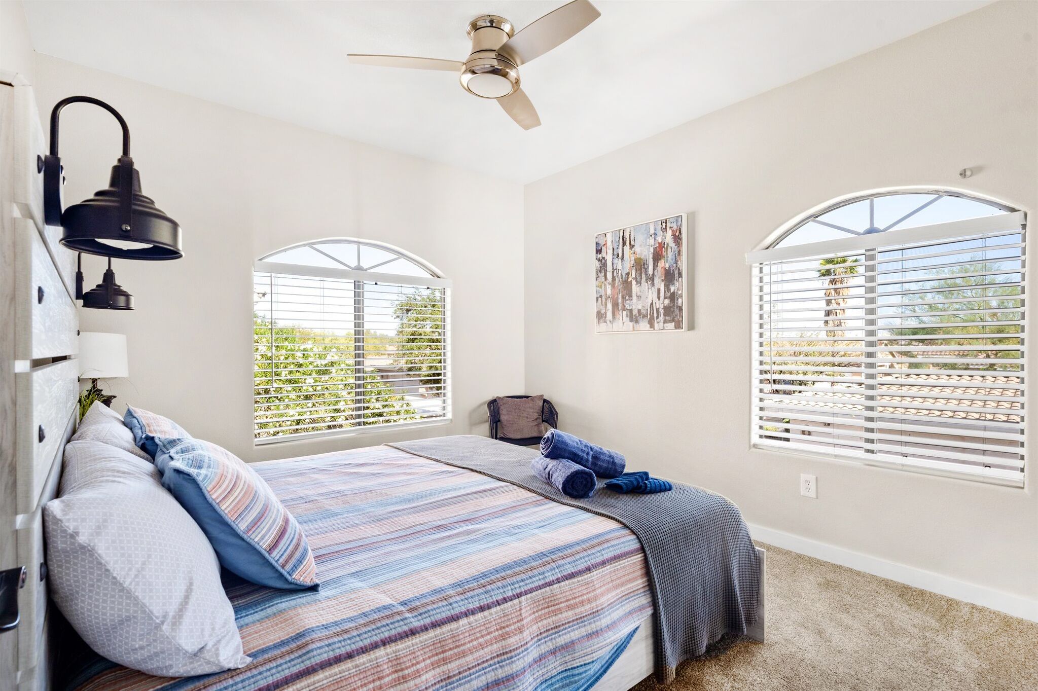A bedroom with a bed, a ceiling fan, and two windows with blinds.