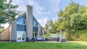 A modern house with a brick exterior, a large chimney, and a patio area with outdoor furniture. - Charming Villa Situated on the Water (De Koog)