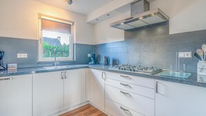 A modern kitchen with white cabinets, a stainless steel range hood, and a window providing natural light. - Charming Villa Situated on the Water (De Koog)
