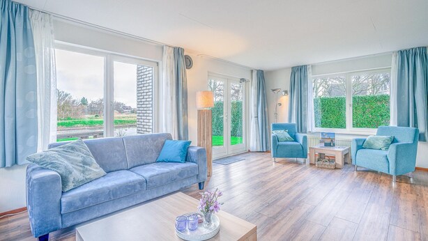 A spacious living room with a blue sofa, a coffee table, and a blue armchair. - Charming Villa Situated on the Water (De Koog)