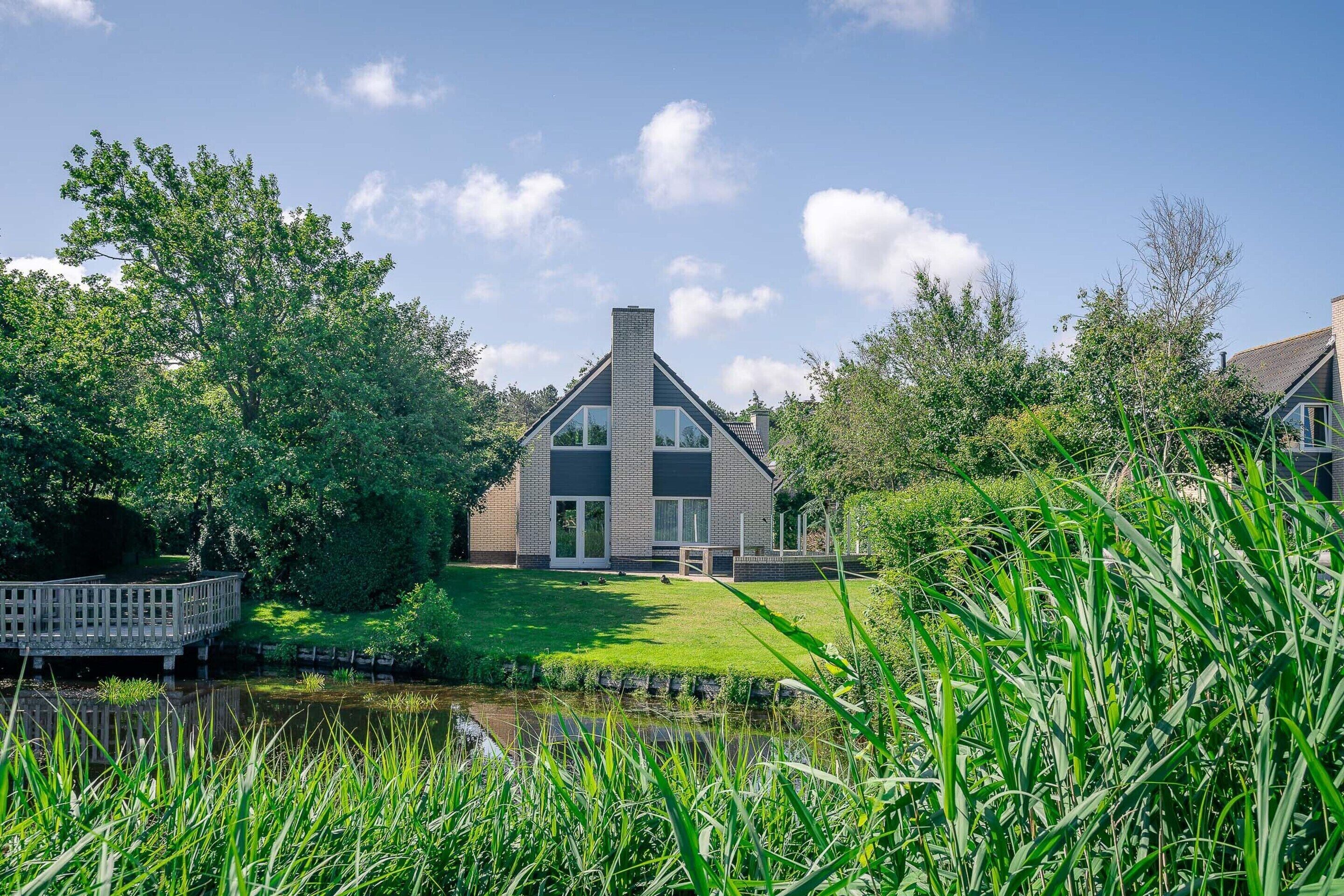 A modern house with a large glass window, a brick chimney, and a grassy lawn.