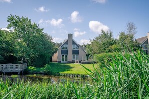 A modern house with a large glass window, a brick chimney, and a grassy lawn. - Charming Villa Situated on the Water (De Koog)