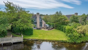 A house with a large lawn, a wooden deck, and a pond. - Charming Villa Situated on the Water (De Koog)