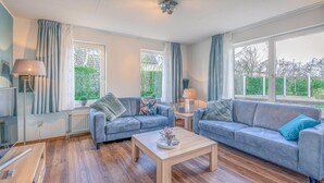 A modern living room with two grey sofas, a wooden coffee table, and a large window with curtains. - Charming Villa Situated on the Water (De Koog)