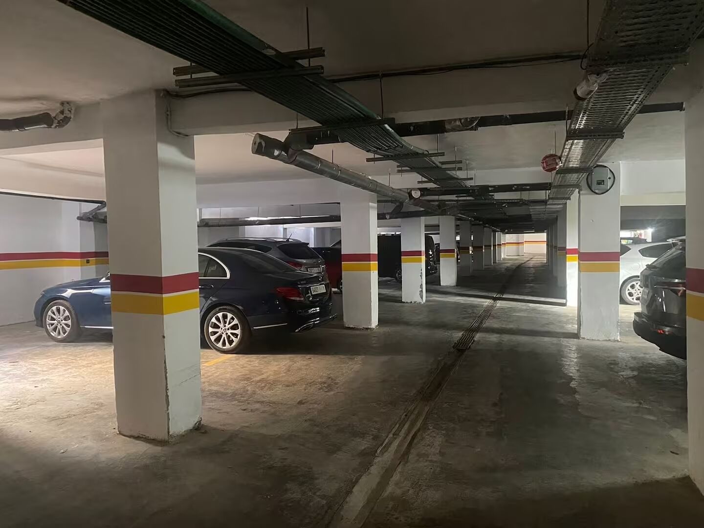 Een ondergrondse parkeergarage met witte pilaren, gele en rode strepen, en geparkeerde auto's.