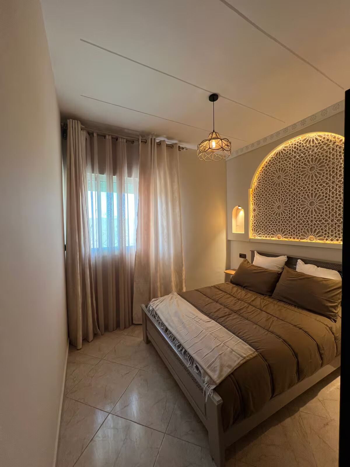 Ein Schlafzimmer mit Bett, Vorhängen, einer Wand mit Muster und einer Pendelleuchte.
