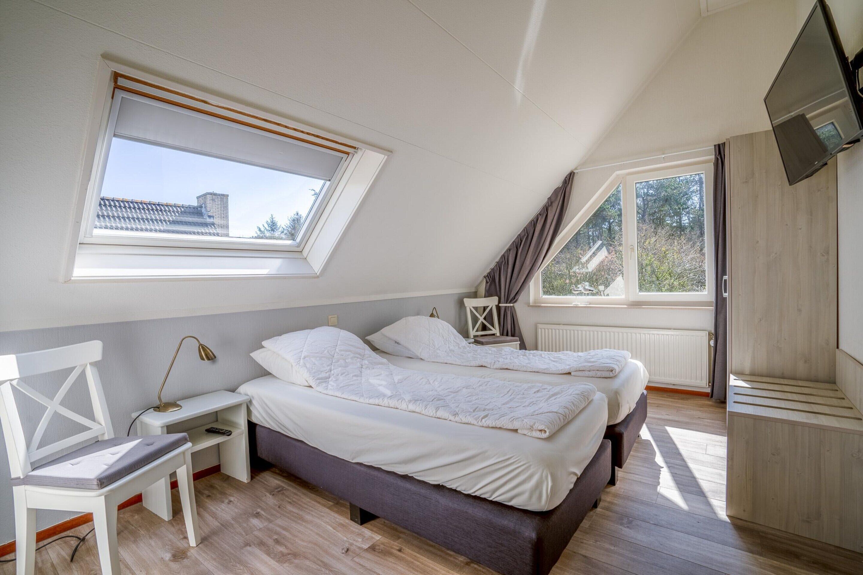 A bedroom with two beds, a desk, a chair, and a TV.
