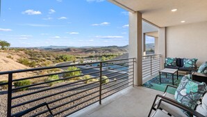 A balcony with a view of a desert landscape, a pool, and outdoor furniture.