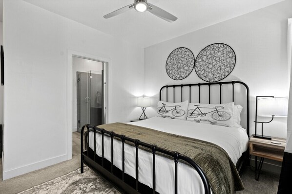 Une chambre à coucher comprenant un lit, une table de chevet, une lampe, un ventilateur de plafond et deux œuvres d’art murales.