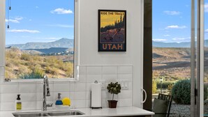 A kitchen with a large window offering a view of mountains and a poster of a bicycle on the wall.