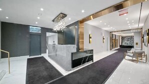 A modern reception area with a marble counter, a chandelier, and a seating area with a sofa and armchairs.