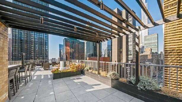 A rooftop patio with outdoor seating, a pergola, and a city view.