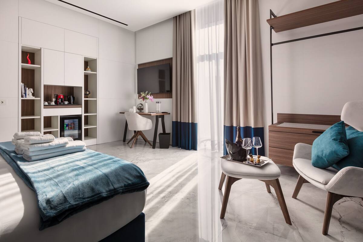 A modern hotel room with a bed, a desk, a chair, and a wardrobe.