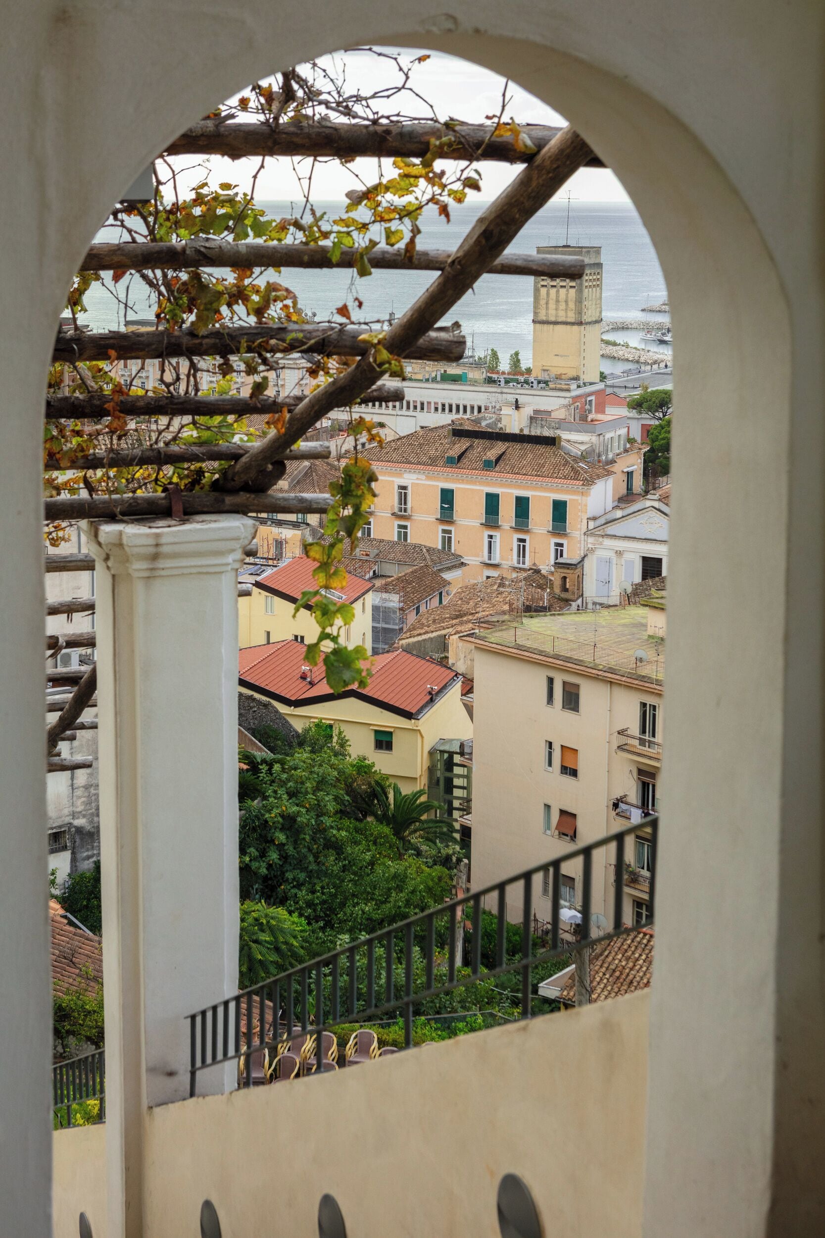Vista a través de un arco con edificios, un balcón y barandilla.