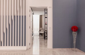 A modern interior with a hallway leading to a dining area, a clear view of the dining space, and a decorative red object on a pedestal. - ViaRomaHome (Salerno)