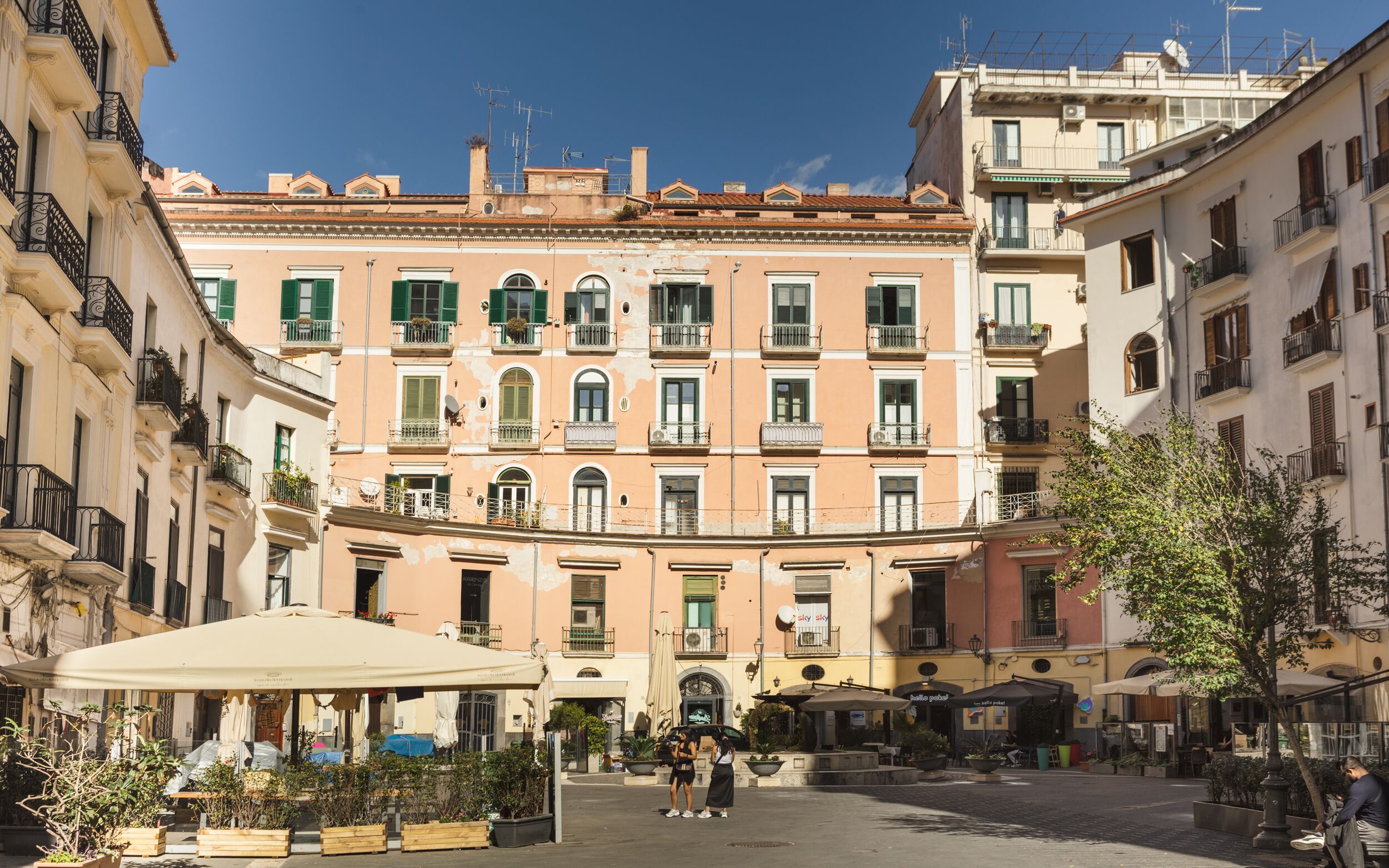 A street view with a row of multi-story buildings, outdoor seating, and a clear sky.