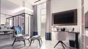 A modern hotel room with a large TV, a seating area with chairs, a desk, and a view of the outdoors. - ViaRomaHome (Salerno)