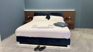 A modern hotel room with a large bed, wooden headboard, marble flooring, and a nightstand with a lamp. - ViaRomaHome (Salerno)