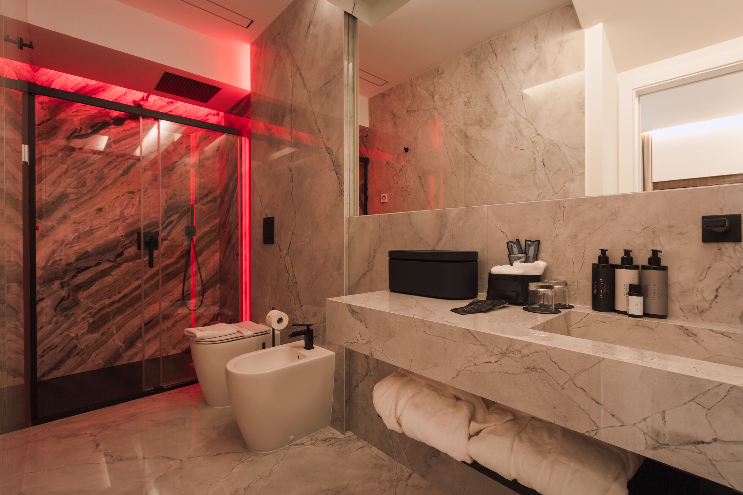 Ein modernes Badezimmer mit Marmorwaschtisch, Toilette und Duschbereich mit roter Beleuchtung.