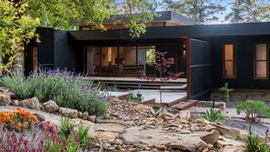 Een modern huis met een grote glazen deur, een pad van stenen en diverse planten.