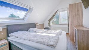 Een slaapkamer met twee bedden, een dakraam, een raam en een houten kast.