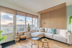 Ein modernes Wohnzimmer mit großem Fenster, einem Ecksofa, einem kleinen runden Tisch und dekorativen Vasen.