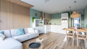 Un salon moderne comprenant un canapé, une table à manger avec des chaises, un coin cuisine avec des placards et des appareils électroménagers, et un mur en bois à lattes.