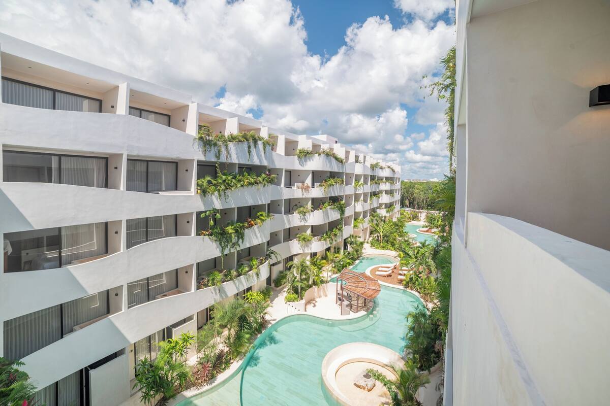 Un hotel moderno con numerosi balconi, una piscina e una vegetazione rigogliosa.