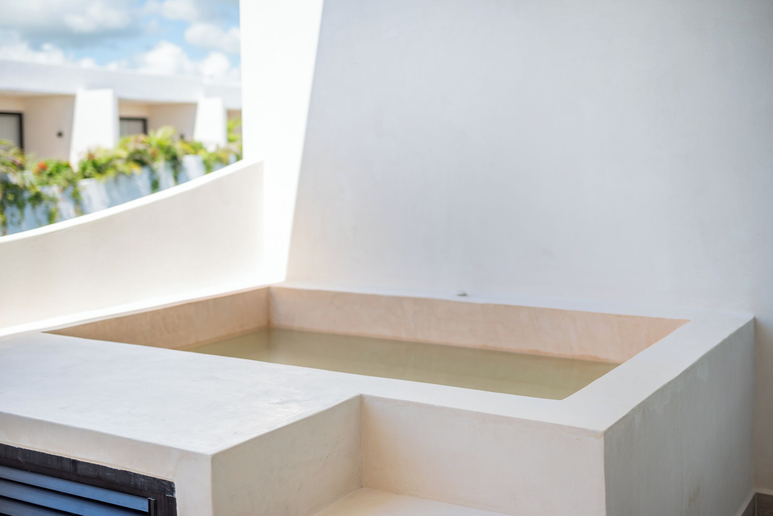 A modern, minimalist bathroom with a large bathtub and a window overlooking a garden.