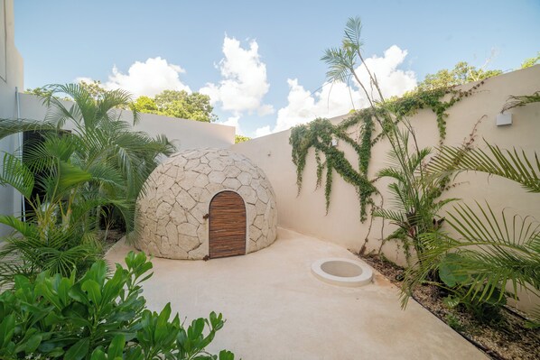 A modern outdoor space with a stone dome structure, surrounded by lush greenery and a clear sky. - Emmare (Tulum)