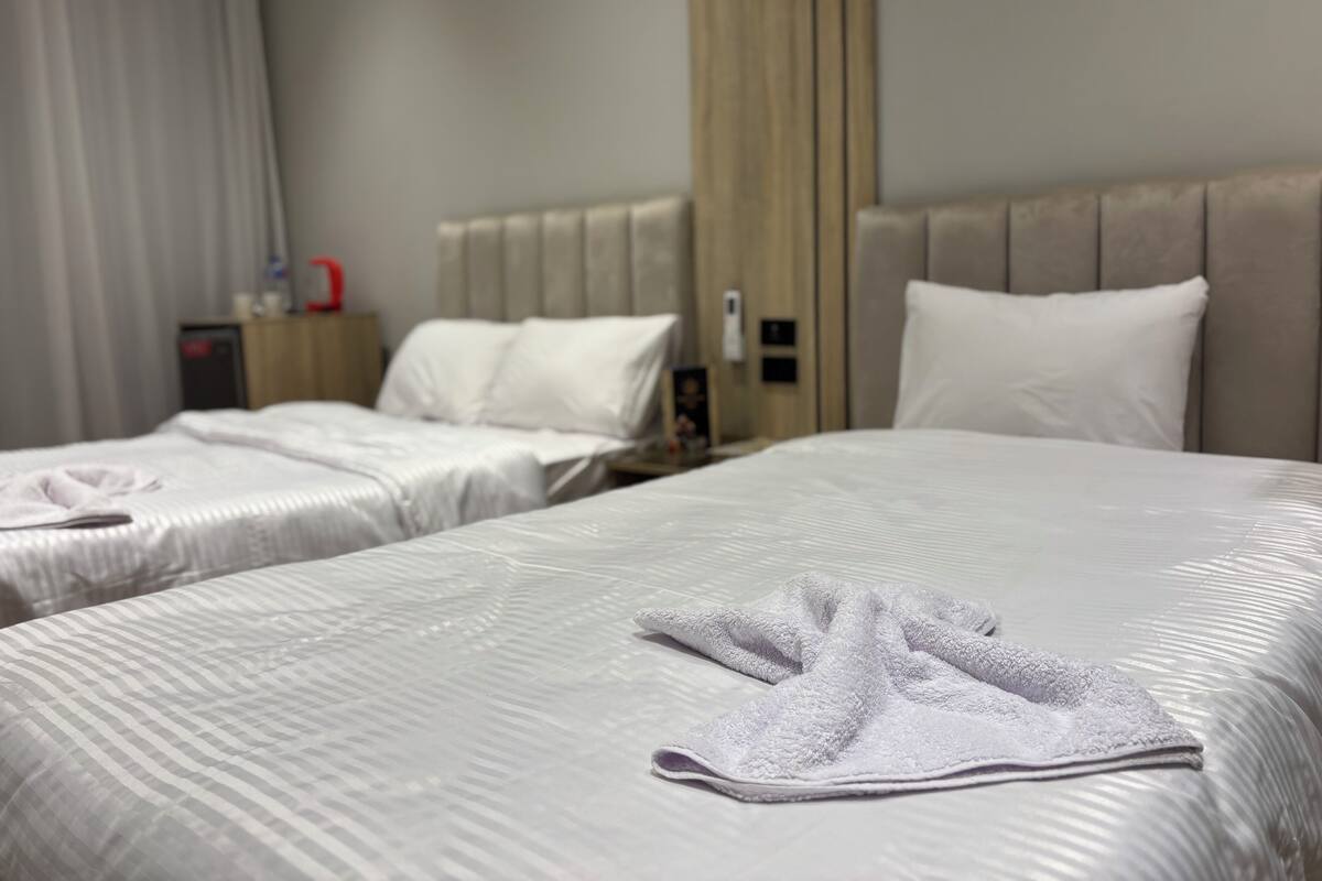 Hotellihuone, jossa on kaksi sänkyä, puinen pääty ja yöpöytä, jossa on lamppu.
