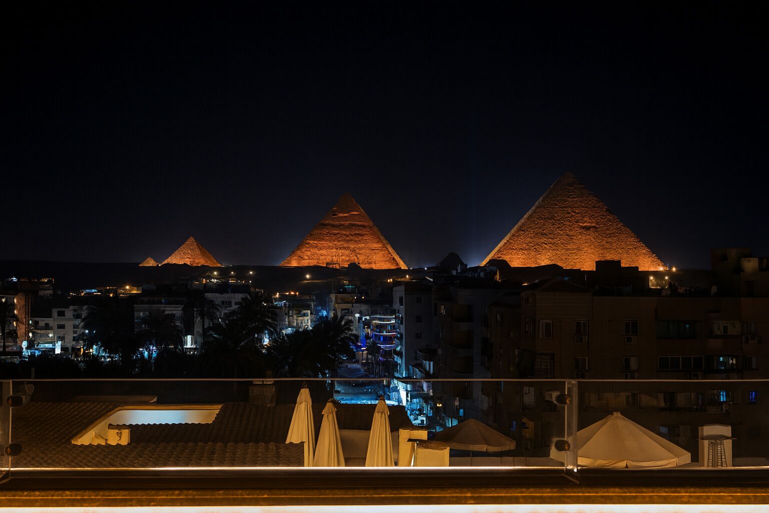 A nighttime view of the Pyramids of Giza with illuminated structures and surrounding buildings.