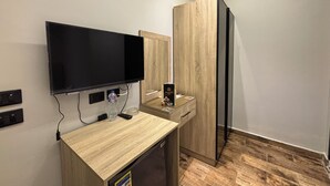 Una habitación de hotel moderna con televisión de pantalla plana montada en la pared, un escritorio de madera con un vaso de agua, un control remoto y una nevera.