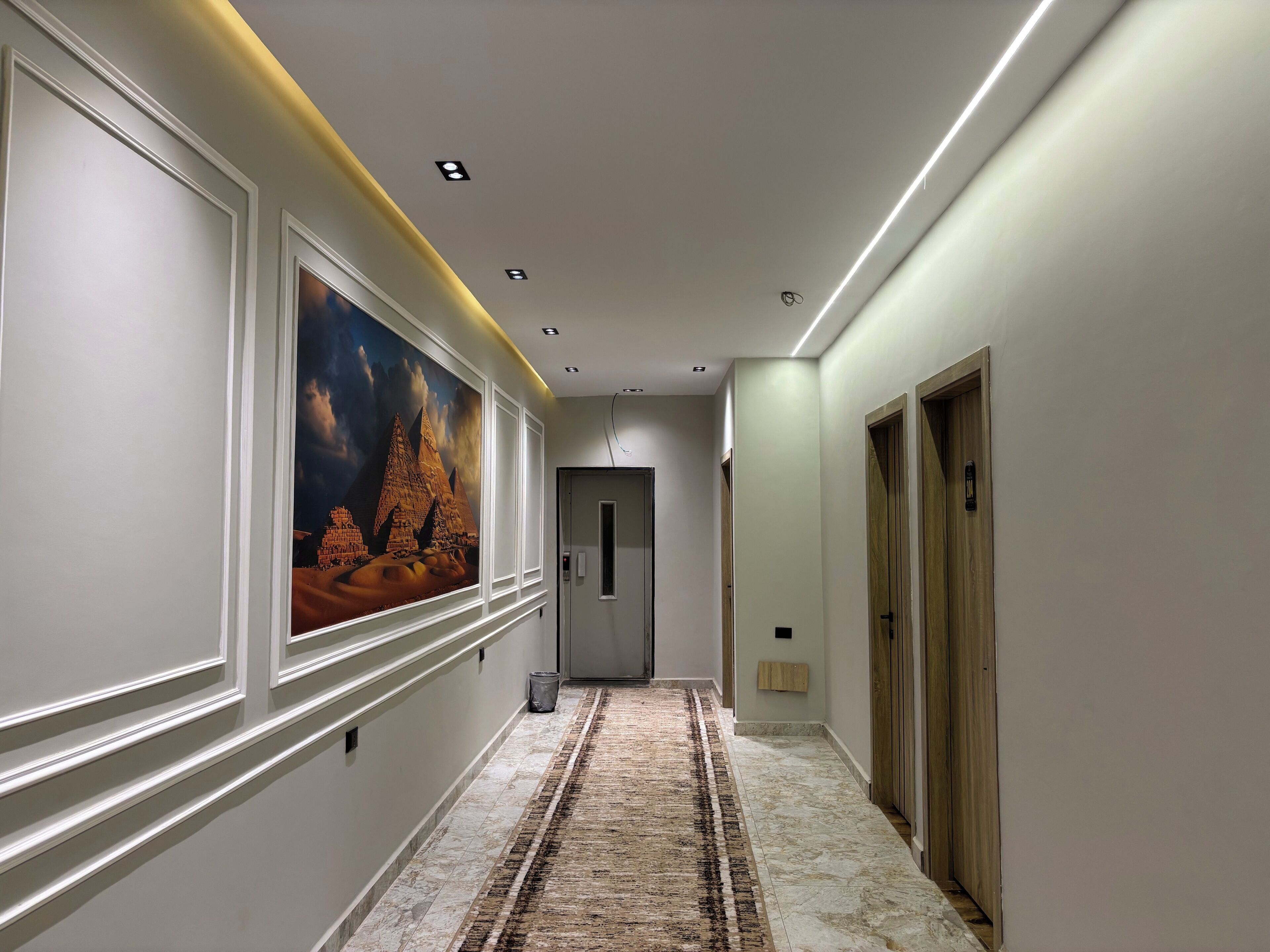 A hallway with a marble floor, a large wall mural, and wooden doors.
