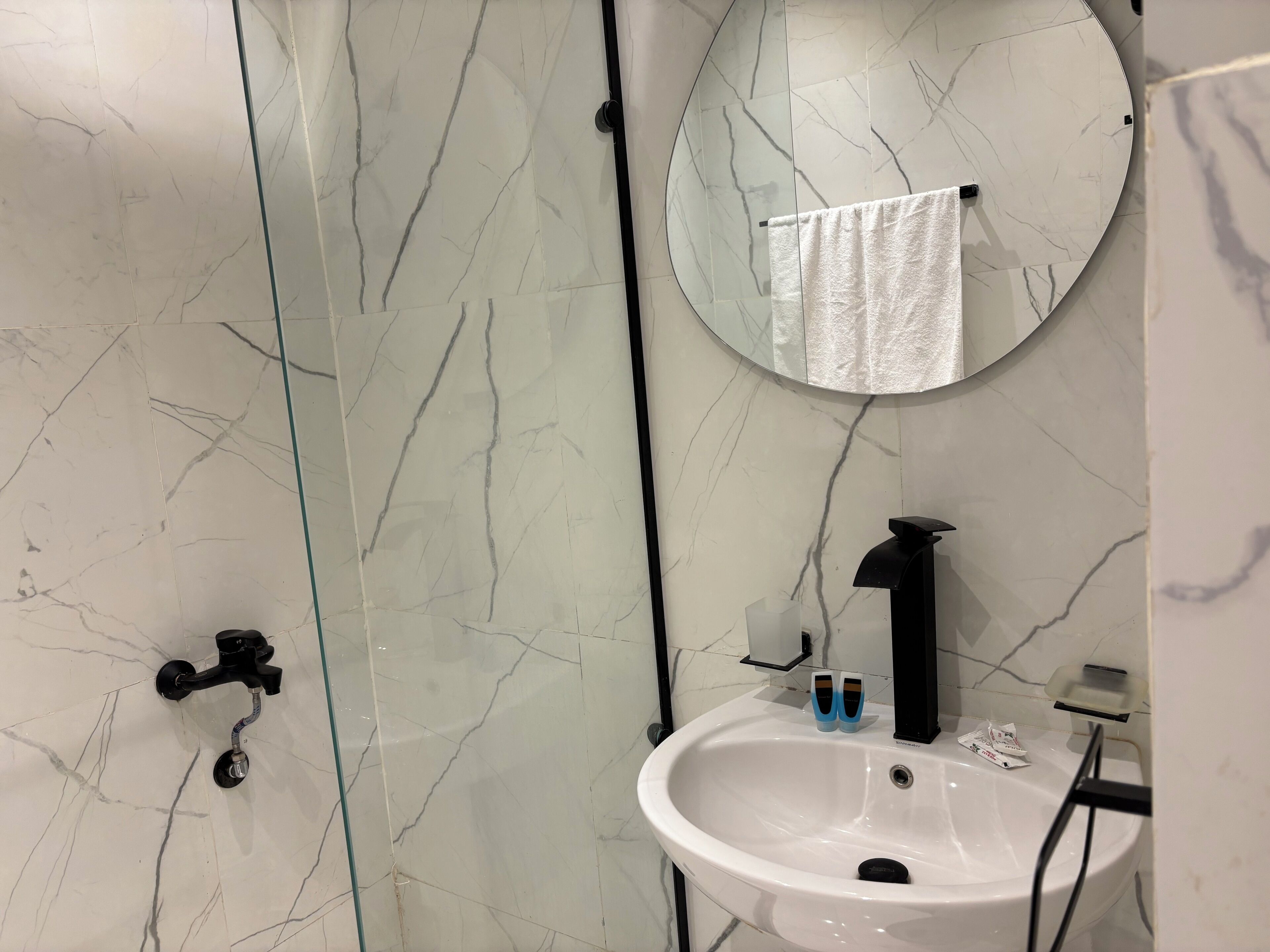 A bathroom with a white marble sink, a black faucet, a mirror with a towel hanging, and a glass shower door.