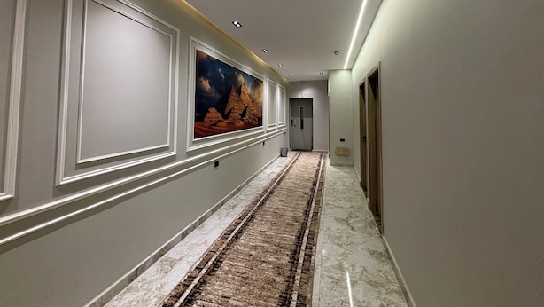 Un pasillo con piso de mármol, obras de arte enmarcadas, iluminación empotrada y una puerta al final.